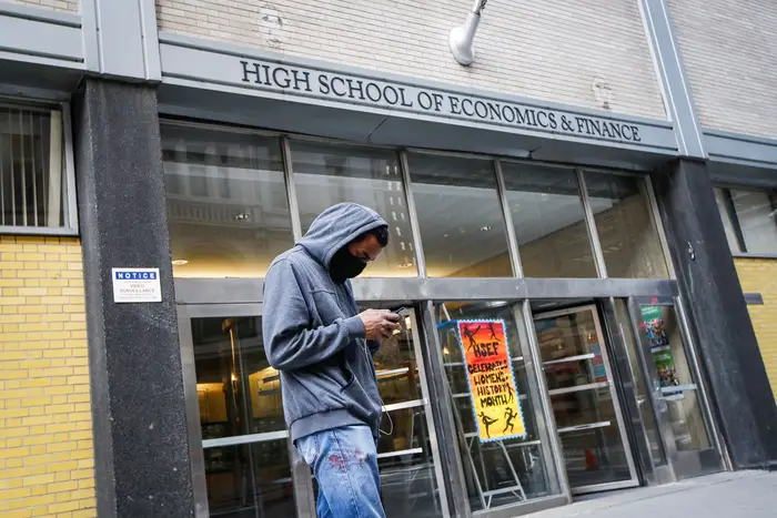 A pedestrian wears a face mask while standing outside the High School of Economics & Finance closed due to coronavirus concerns, in New York., on March 16, 2020